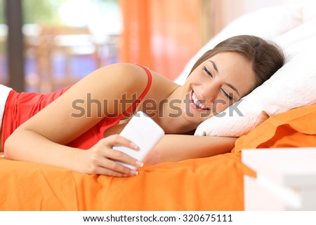 Happy teen using a smart phone in the bed at home with an orange background