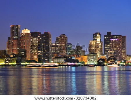 Boston downtown skyline panorama with skyscrapers over water with reflections at dusk illuminated with lights. 