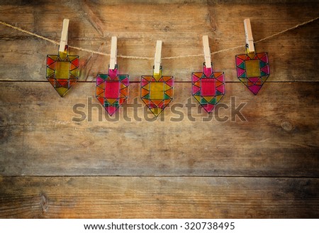 image of jewish holiday Hanukkah with Stained-glass colorful dreidels (spinning top)  hanging on a rope over wooden background