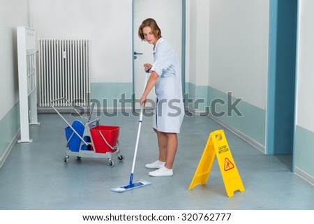 Young Female Janitor Mopping Floor With Wet Caution Sign And Cleaning Equipments