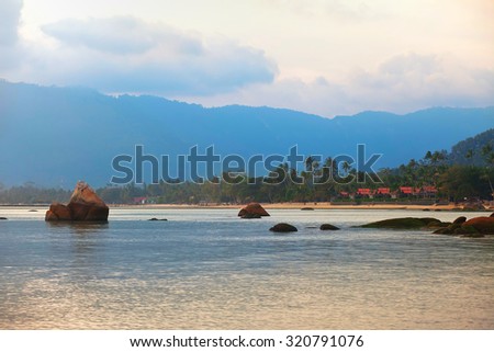 view on a tropical beach, stones in the water and the mountain
