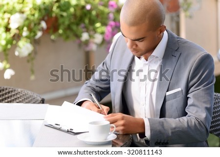 No minute without writing. Top view of pleasant handsome businessman making notes and drinking coffee while sitting at the table