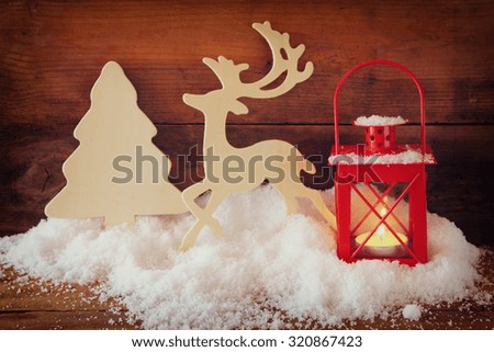 christmas background with red lantern, wooden decorative reindeer and tree on the snow over wooden background