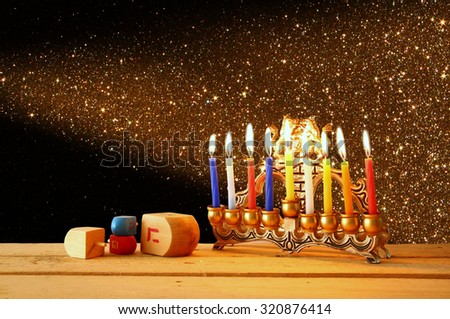 low key image of jewish holiday Hanukkah with menorah (traditional Candelabra) and wooden dreidels (spinning top). glitter overlay 