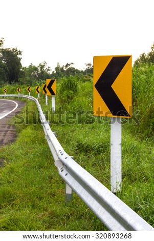 Traffic sign indicating a curve to the left and straight ahead a row rural forest grass.