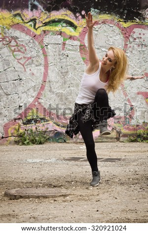Young girl dancing on graffiti background. Dancing and urban culture concept. Film grain effect
