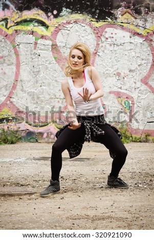 Young girl dancing on graffiti background. Dancing and urban culture concept. Film grain effect
