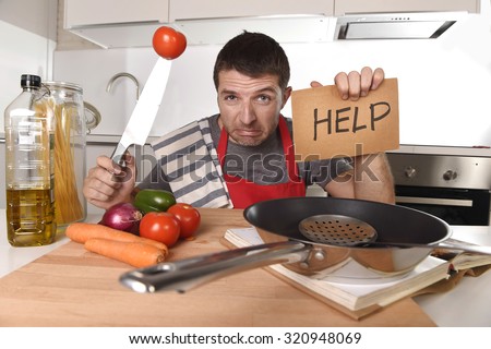 young terrified man at home kitchen wearing cook apron showing help sign looking desperate in stress holding knife with tomato in domestic mess cooking concept