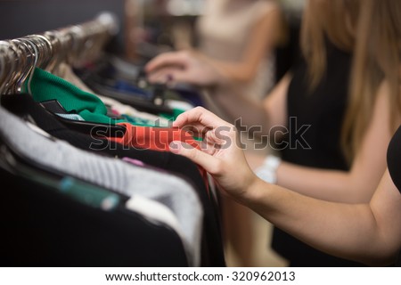 Young beautiful women shopping in fashion mall, choosing new clothes, looking through hangers with different casual colorful garments on hangers, close up of hands Royalty-Free Stock Photo #320962013