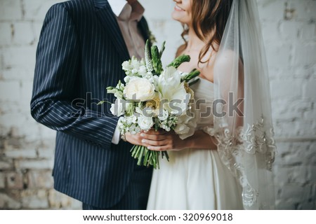 the bride and groom are holding a bouquet of white flowers and greenery in the background Vintage wall of white brick