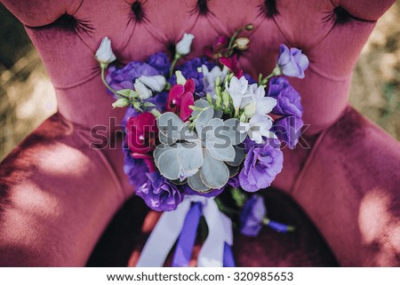 bridal bouquet of red, blue, purple flowers and greenery lies in an old chair