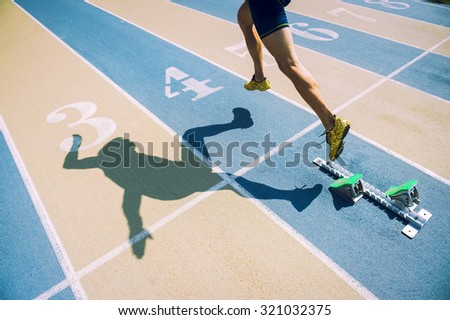 Athlete in gold shoes sprinting from the starting blocks over the starting line of a race on a blue and tan running track 