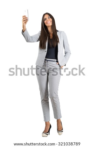 Young smiling business woman taking selfie with mobile phone.  Full body length portrait isolated over white studio background. 