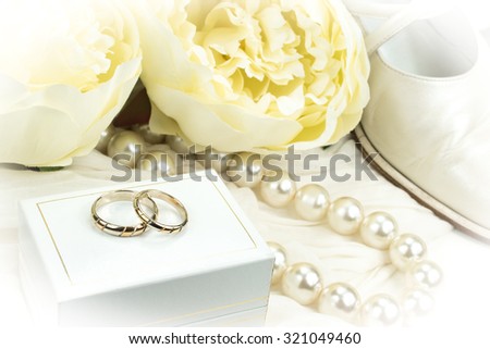 Wedding concept: pair of golden wedding rings on white box, pearl necklace, shoes and peony flowers.