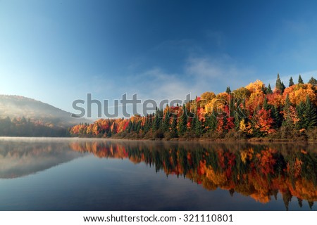 Autumn forest reflected in water. Colorful autumn morning in the mountains. Colourful autumn morning in mountain lake. Colorful autumn landscape. Parc national Mont Tremblant. Quebec. Autumn in Canada Royalty-Free Stock Photo #321110801