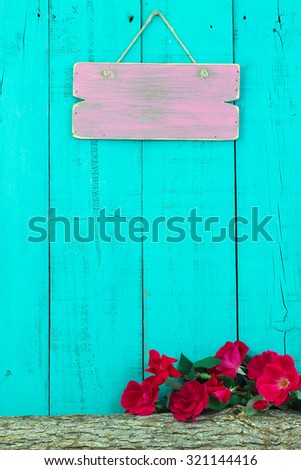 Blank pink sign hanging over log with red flowers with antique teal blue wood background