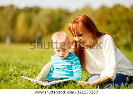 Picture of beautiful woman with son sitting down on green grass field and read fairytale in park