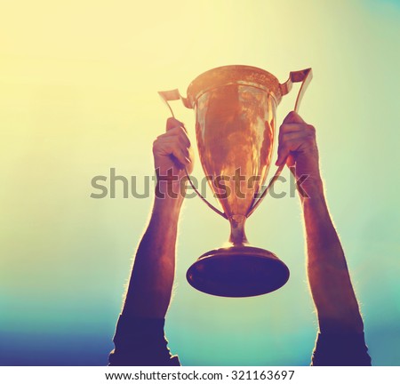a man holding up a gold trophy cup as a winner in a competition toned with a retro vintage instagram filter effect app or action (backlit with the sun) Royalty-Free Stock Photo #321163697