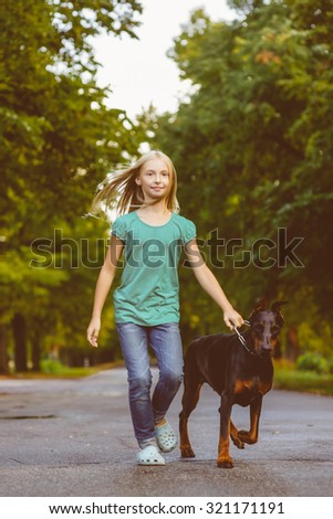blonde girl walking with the dog or doberman in summer park. Warm toned photo
