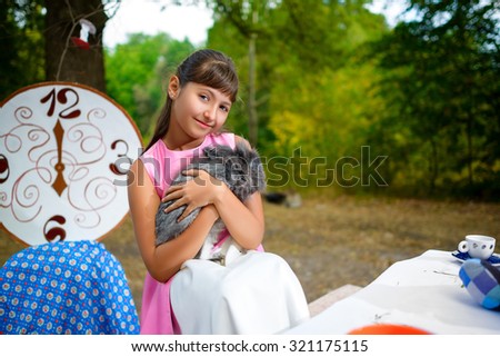 Girl sits at table and holding a rabbit. Alice in Wonderland concept