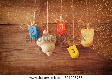 image of jewish holiday Hanukkah with wooden colorful dreidels (spinning top) hanging on a rope over wooden background with glitter overlay 