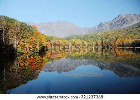 Autumn lake Scenery. Forests of colorful foliage reflected on the smooth water of Kagami Ike ( Mirror Pond ) with Mountain Togakushi in the distant background ~ Beautiful landscape of Nagano, Japan 