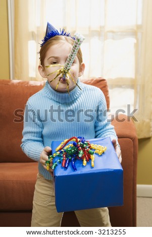 Caucasian girl blowing noisemaker and holding gift.