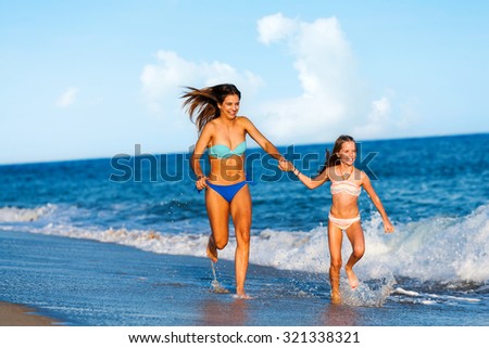 Action portrait of two young happy women running and splashing water  along beach.