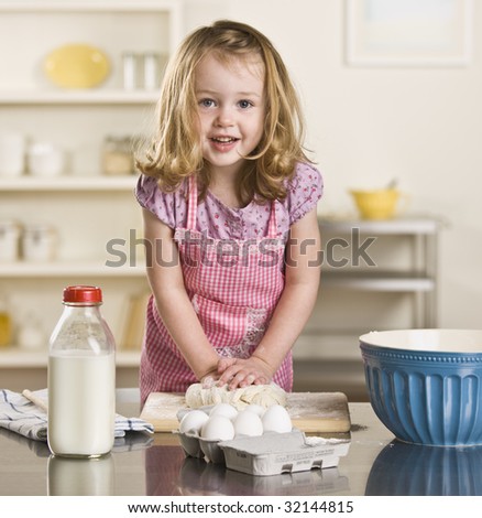 Cute blond little girl making bread in the kitchen. Milk bottle, bowl and eggs on the counter. Square