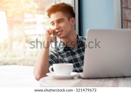 Businessman using mobile phone while lookingat laptop on wooden table in coffee shop
