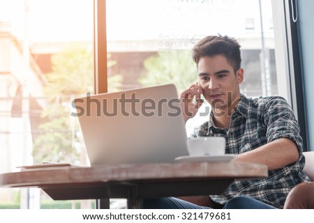 Businessman using mobile phone while lookingat laptop on wooden table in coffee shop