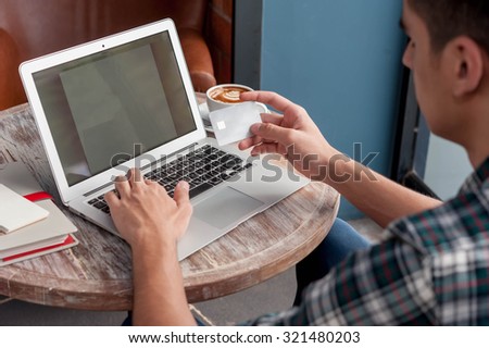 Businessman look at credit card while using laptop on wooden table in coffee shop