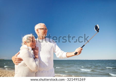 age, travel, tourism, technology and people concept - happy senior couple with smartphone on selfie stick taking picture on summer beach