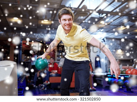 people, leisure, sport and entertainment concept - happy young man throwing ball in bowling club at winter season