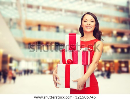 christmas, holidays, valentine's day, celebration and people concept - smiling woman in red dress with gift boxes over shopping center background