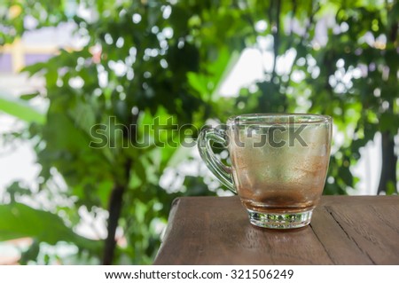 Single empty glass of coffee on wood table with blur green leafs background
