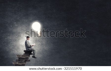 Young businessman sitting on pile of old books with one in hands