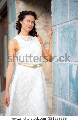 beautiful middle-aged woman in a white summer  dress near the old wall of the ancient house