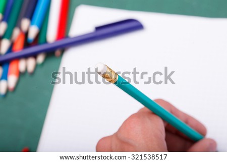 Set of colorful wooden pencils yellow green red pink orange blue and brown lying in row on table with white paper sheet with writing human hand copy space, horizontal picture