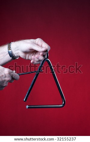 A musical triangles being played by hands isolated against a red background in the vertical format with copy space.