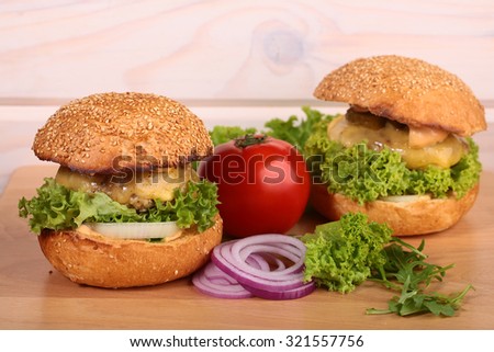 One big tasty appetizing fresh burger of green lettuce red tomato cheese bacon slice meat cutlet violet onion and white bread bun with sesame seeds on wooden table closeup, horizontal picture