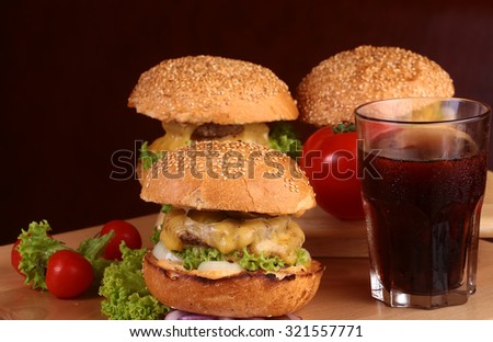 One big tasty appetizing fresh burger of green lettuce cheese bacon slice meat cutlet and white bread bun with sesame seeds and potato chips on wooden table and cola, horizontal picture