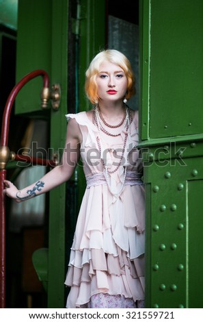 Beautiful feminine blonde girl in a vintage dress out of a retro train at the station