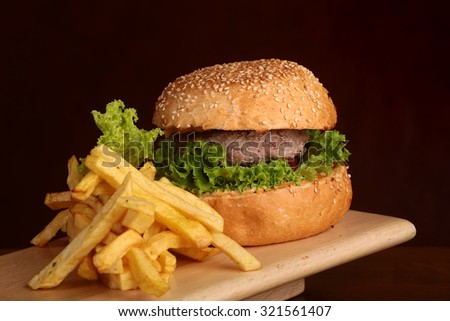 One big tasty appetizing fresh burger of green lettuce red tomato cheese and bacon slice meat cutlet and white bread bun with sesame seeds and potato chips, horizontal picture