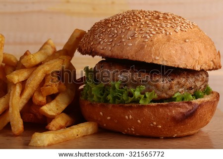 Big tasty appetizing fresh burger of green lettuce cheese bacon slice meat cutlet and white bread bun with sesame seeds and potato chips on wooden table and potato chips, horizontal picture