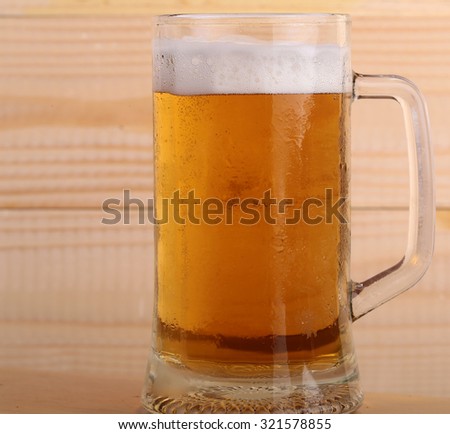 Closeup of one big glass goblet full of light tasty frothy alcoholic beverage of beer standing on wooden background, square picture