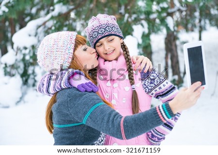 Mom and daughter are photographed in a winter forest, family values. Two girls make a photo on the flatbed in a snowy park