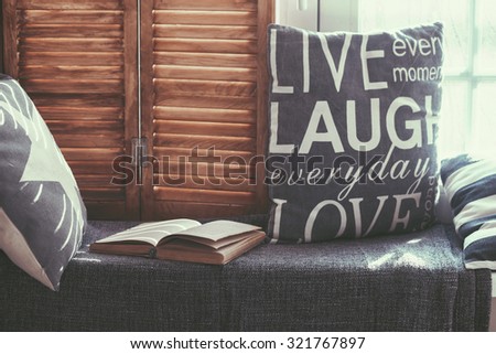 Warm and cozy window seat with cushions and a opened book, light through vintage shutters, rustic style home decor. Royalty-Free Stock Photo #321767897