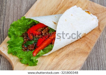 Tortilla with meat, salad and pepper on the wood background