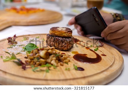 Man using mobile phone take a picture of Grilled Fillet of Veal topped with Foie Gras.